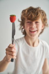 Funny child with strawberry on top of knife