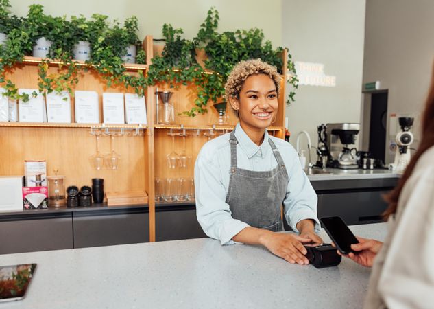 Happy woman behind counter in coffee shop taking customer payment