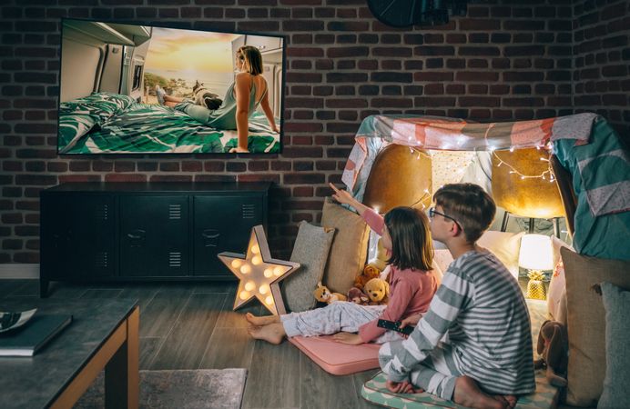 Two children in pajama sitting while watching television film on living room. Domestic life concept.