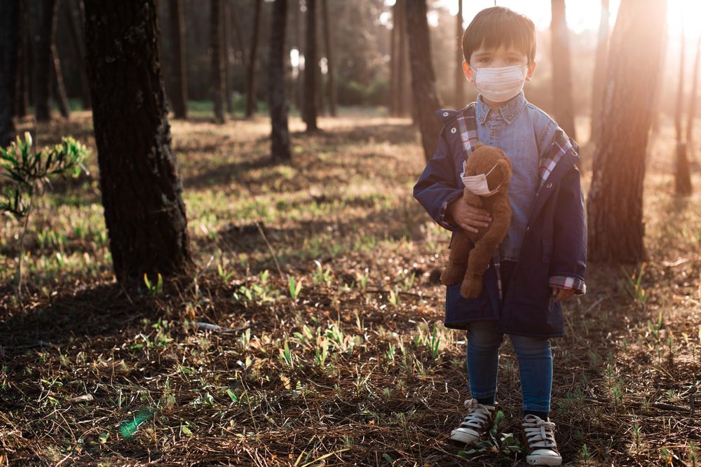 Boy holding stuffed bear and both wearing masks