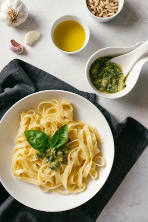 Served plate of pesto pasta next to bowl of sauce on table