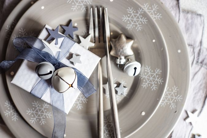 Top view of wrapped Christmas present with bell and star ornament on table setting