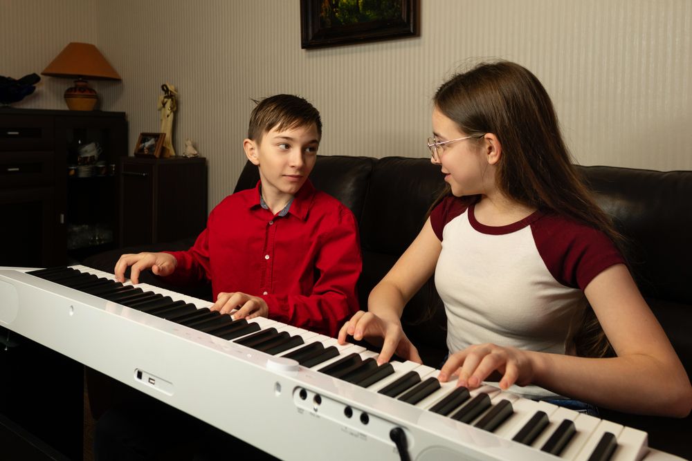 Two children playing the piano together, looking at each other.