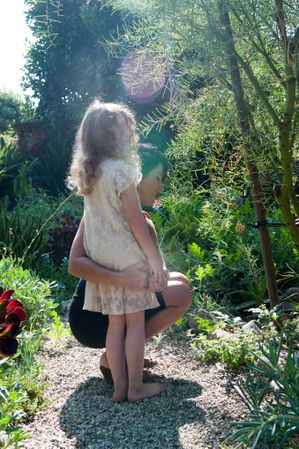 Mother holds daughter around her waist while looking at garden plants