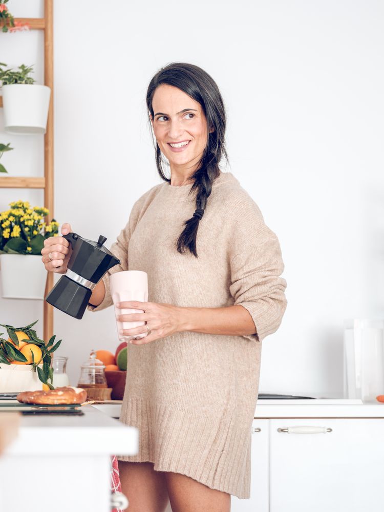 Smiling female pouring coffee from moka pot in kitchen