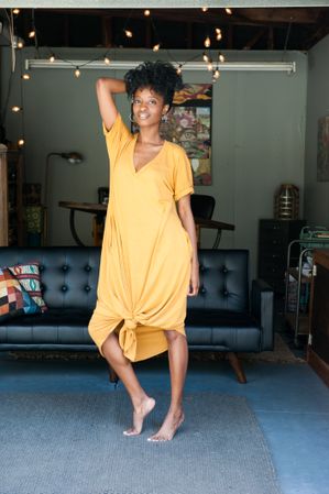 Full length shot of woman with natural hair standing in long yellow dress in front of couch