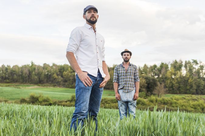 Two men in plaid shirt standing in long grass with forest in background