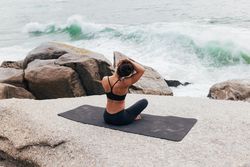Female sitting next to the ocean sitting crossed legged stretching her neck