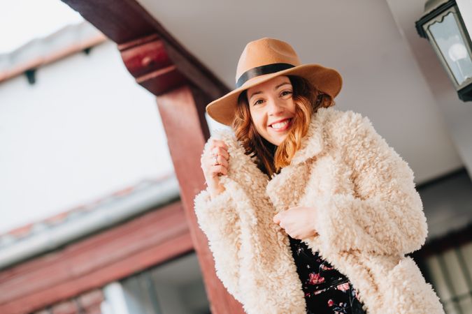 Smiling woman in warm wear standing near building and fence