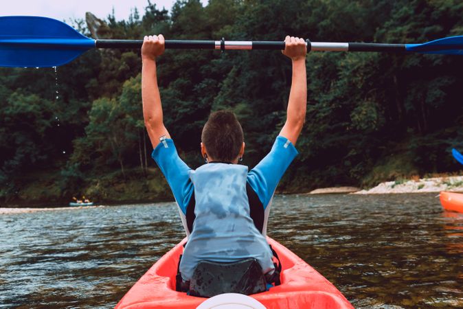 Female kayaking with paddle in raised hands