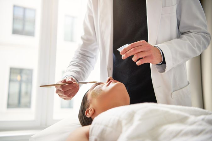 Man in lab coat brushing treatment onto woman’s face