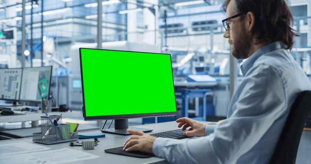 Robotics Engineer Working on a Desktop Computer with Green Screen Chromakey Mock Up Display in a Startup Factory. High Tech Technological Research and Development Company with Autonomous Assembly Line