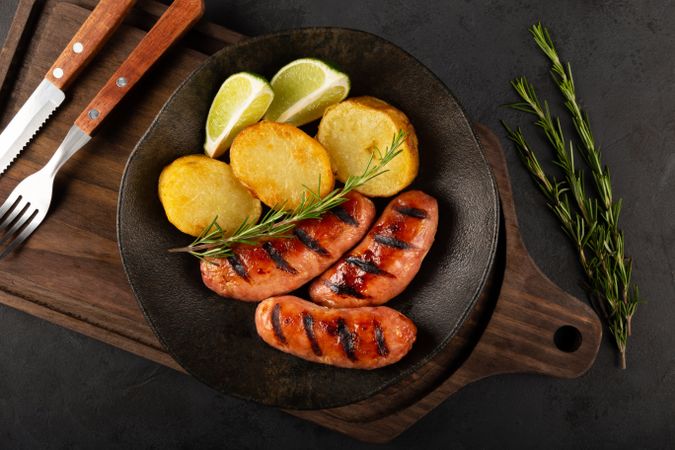 Top view of plate with grilled sausages, potatoes, and lime slices