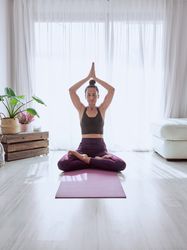 Woman sitting in Padmasana on mat with namaste gesture