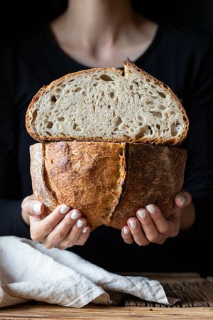 Crop person holding halved seeded bread
