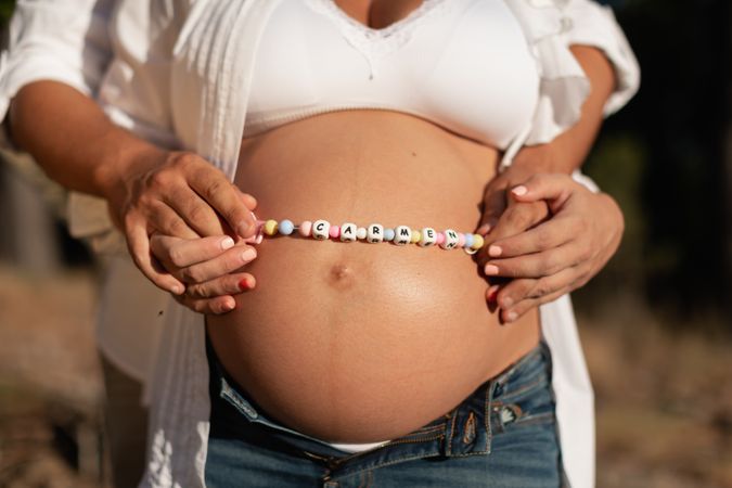 Pregnant woman's belly with beaded necklace with baby name