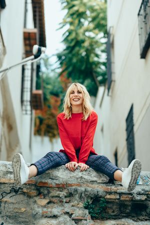 Smiling blond woman sitting on stone wall with her legs out