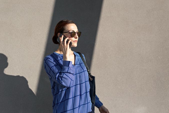 Businesswoman having smartphone conversation near gray wall