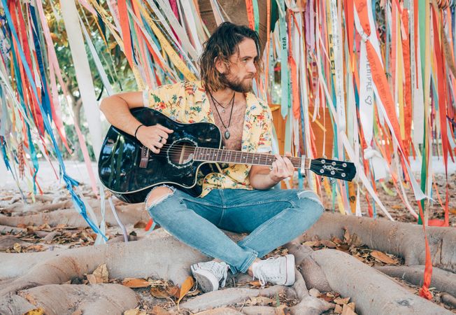 Man sitting under tree playing guitar