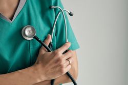 Crop surgeon with stethoscope on light background
