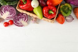 Wicker basket and vegetables on wooden background, top view