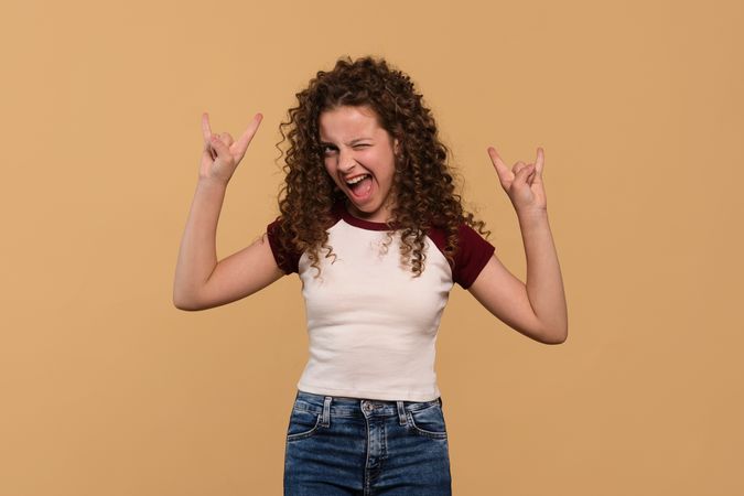 Young girl flashing rock hand signs with enthusiastic expression