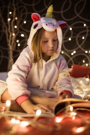 Girl reading book in bedroom decorated with Christmas lights