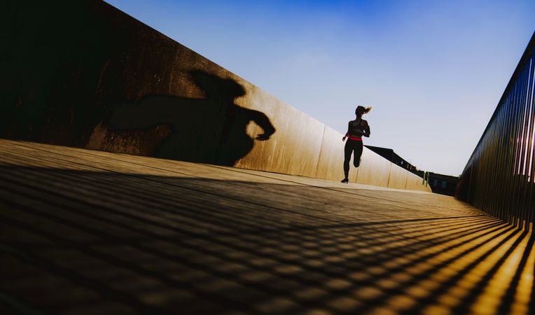 Woman running on walkway in sunny day with blue sky