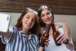 Cheerful girlfriends with beer spending weekend on sofa