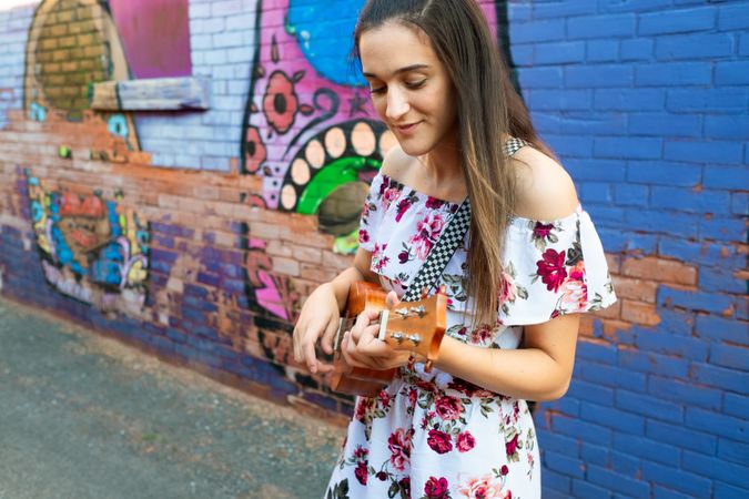 Joyful woman playing ukulele while standing on urban street