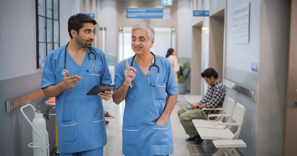 Portrait of Two Indian Male Doctors Walking in Hospital Corridor and Talking while Using a Digital Tablet.