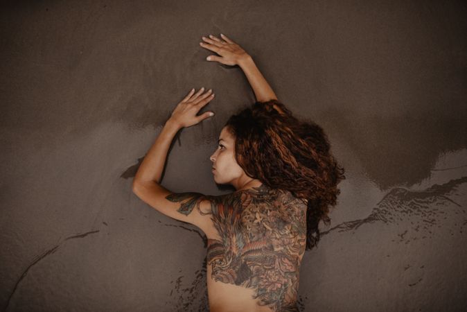 Tattoed woman lying on wet sand