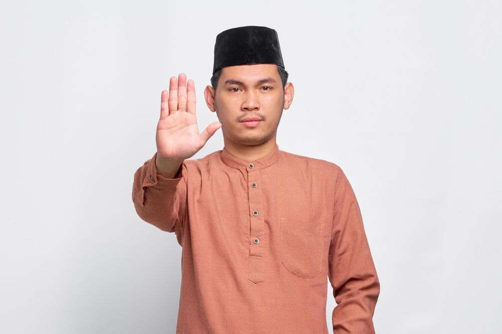 Muslim man in kufi cap with hand up to say “stop”