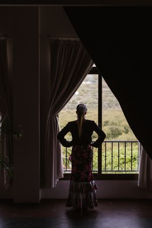 Woman dancer in suit for flamenco standing and looking out window