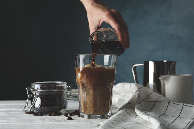 Woman pours a glass of coffee. Composition with ice coffee
