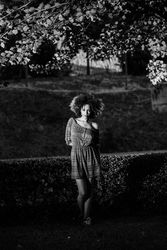B&W shot of woman in dress standing in park looking at camera, vertical
