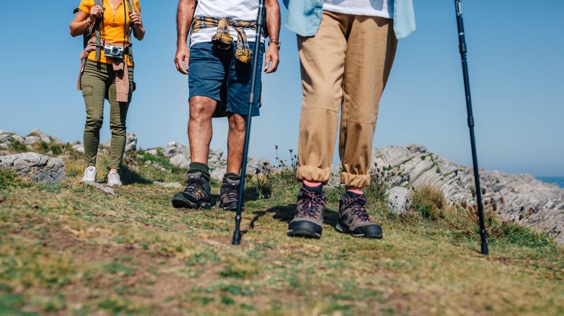 Legs of three hikers with poles on hill by ocean
