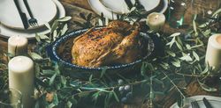 Centerpiece of roast chicken with decorative branches, candles, wide composition