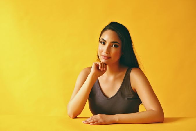 Serious Hispanic woman looking at camera and sitting in yellow room, copy space