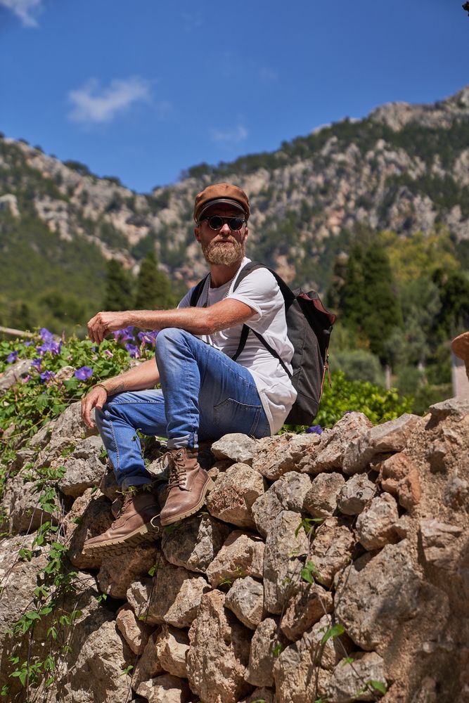 Male tourist sitting on rocky fence in mountains
