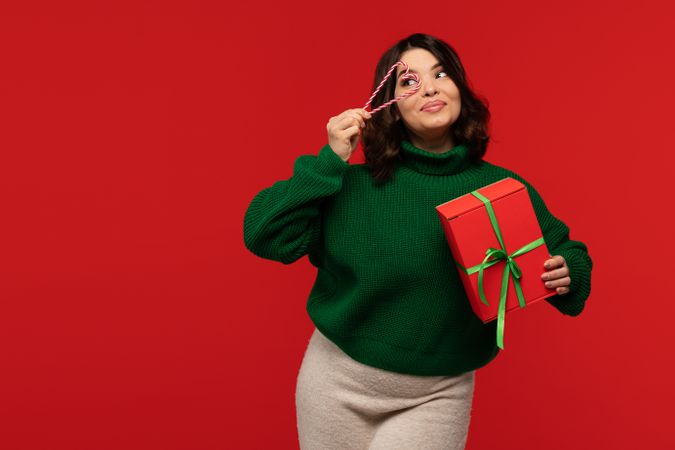 Woman holding gift box and candy cane heart near eye