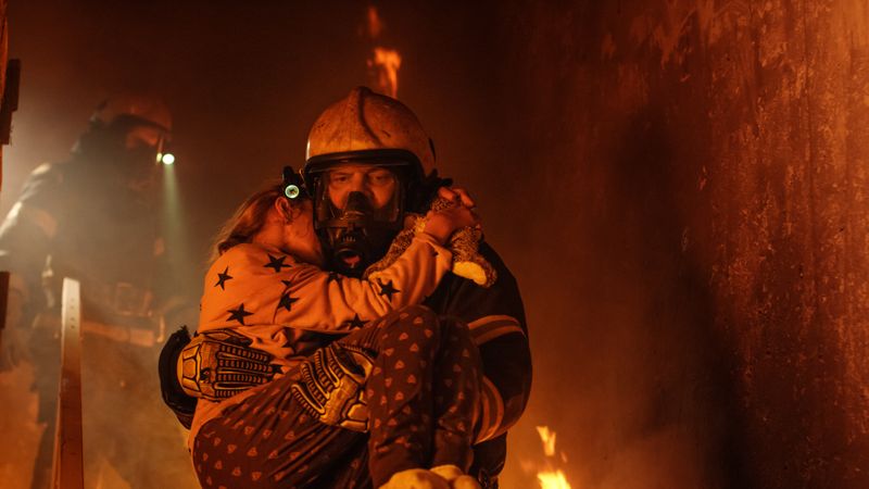 Firefighter escaping burning building with girl in his arms