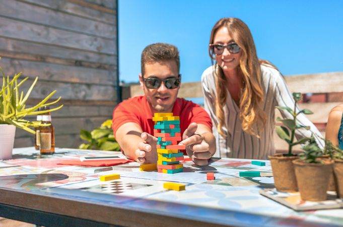 Concentrated young man pushing game piece next to female friend in rooftop party