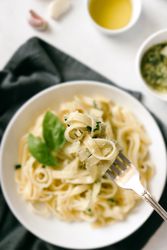 Served plate of pesto pasta next to bowl of sauce on table