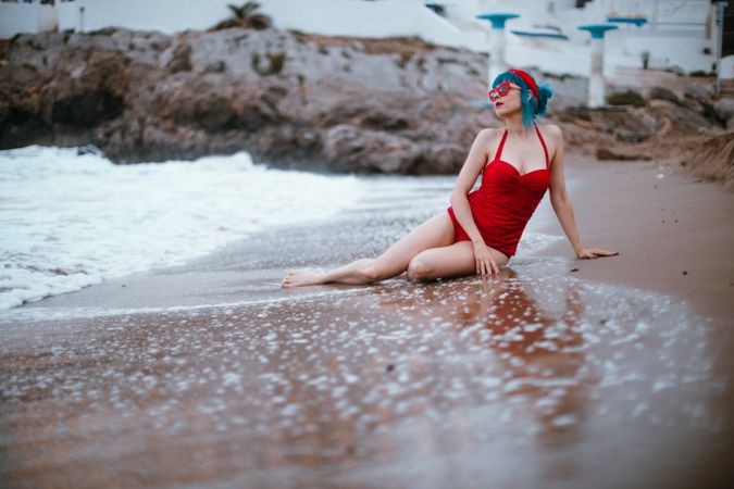 Relaxed woman in bright stylish swimsuit sitting on sandy beach