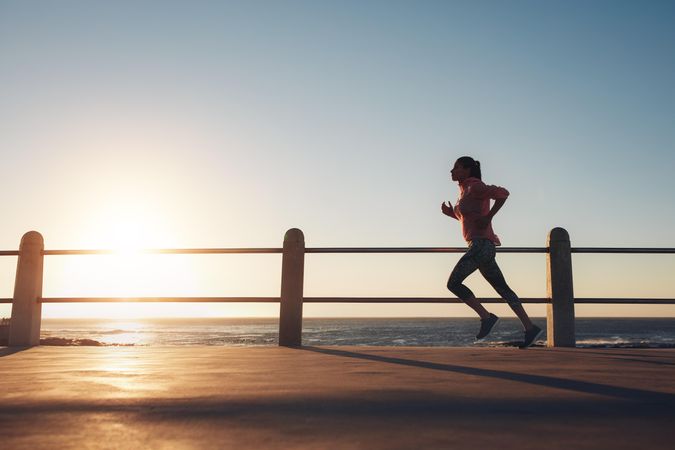 Image of fit sportswoman jogging on a road by the sea during evening