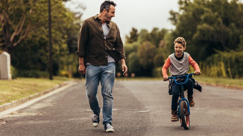 Young boy riding bike with father beside him