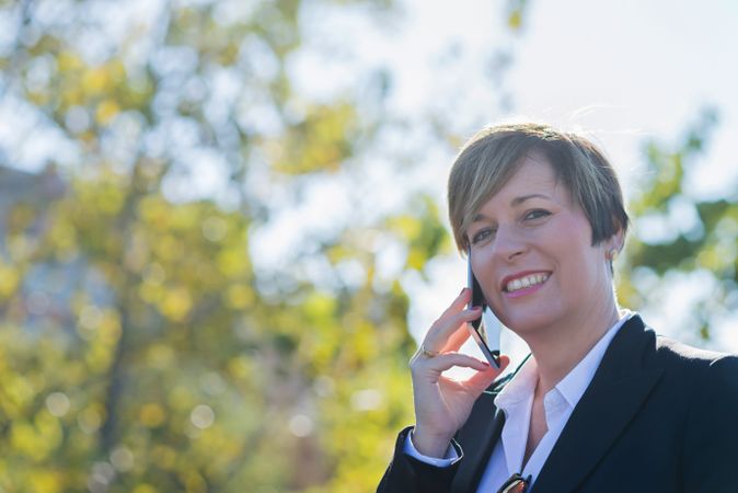 Happy woman standing in park speaking on phone