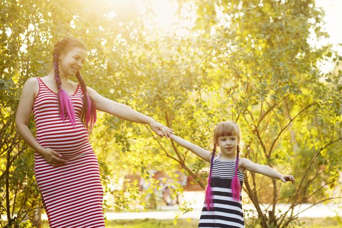 Pregnant woman holding hand of her child in a sunny park