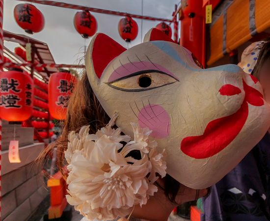 Person wearing Inari-Fox mask celebrating Motomiya-sai festival in Kyoto, Japan